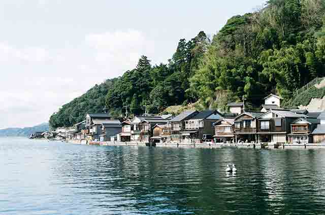穏やかな伊根湾沿いに舟屋と呼ばれる建物がずらりと建ち並ぶ＝2021年3月14日、岩倉しおり撮影